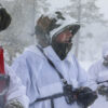Three service members stand together in the snowy woods, dressed in white winter uniforms
