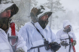 Three service members stand together in the snowy woods, dressed in white winter uniforms